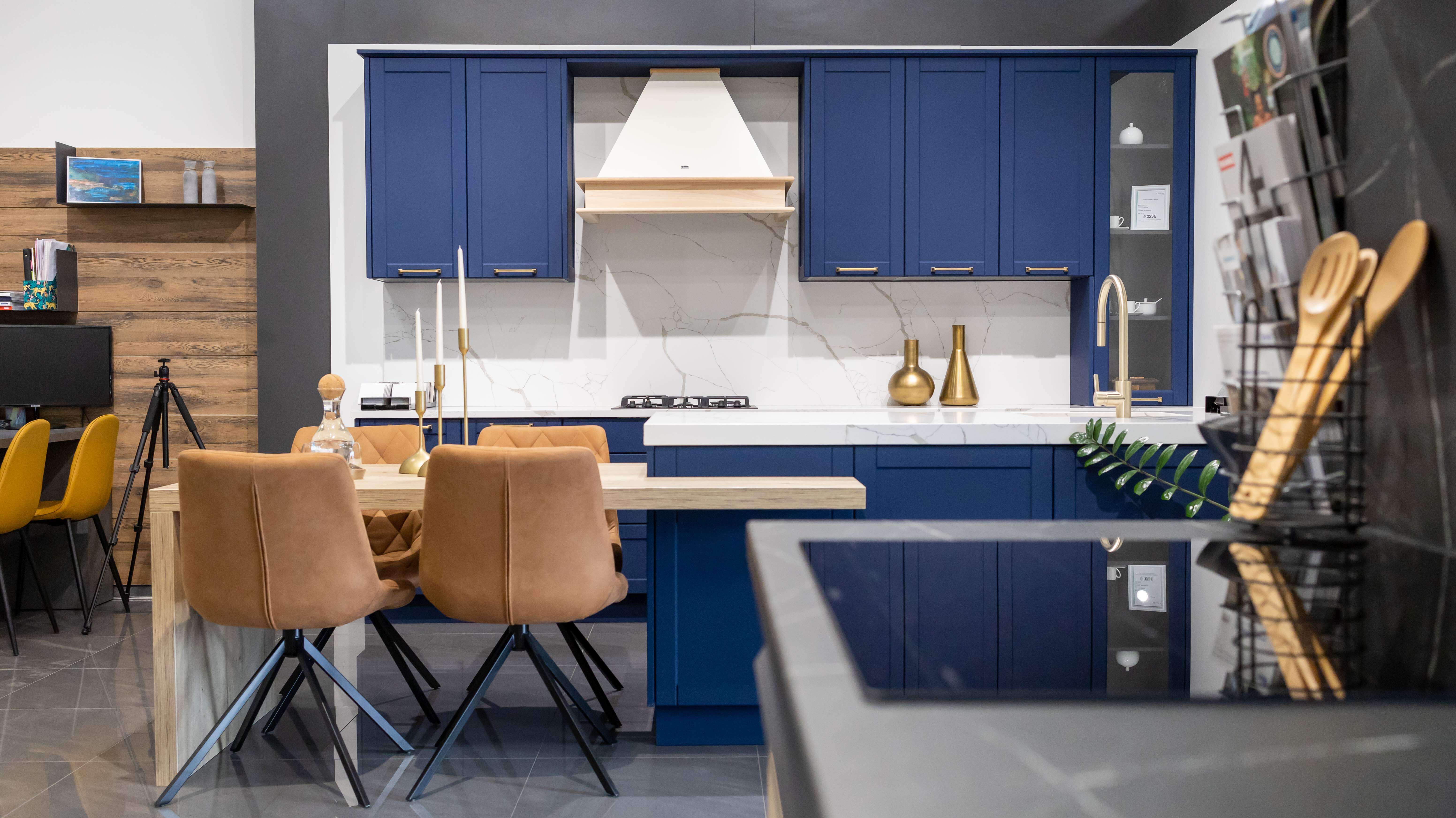 Elegantná kuchyňa s modrými rámovými dvierkami, mramorovou zástenu a zlatými doplnkami, doplnená o pohodlné sedenie a otvorené police s dekoráciami.